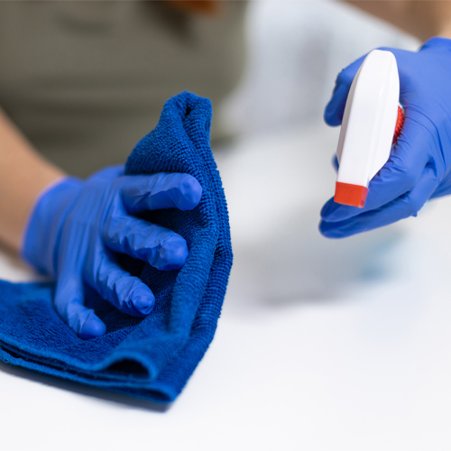 Close up of woman clean house, office or restaurant. A girl in rubber gloves wiped the dust with spray and a blue cloth to clean the dirty table.