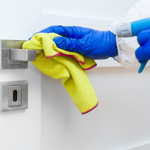 Hand in protective glove with rag cleaning door handle. Covid-19 disinfection concept.